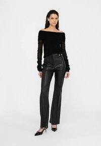 Top noir à épaules dénudées avec manches longues transparentes, associé à un pantalon noir en similicuir taille haute avec un design en lignes et des détails à boutons.