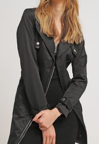 Czarna, lekka kurtka w stylu motocyklowym, z srebrnymi detalami, zamkiem błyskawicznym i ukośnym kołnierzem, prezentująca gładką, błyszczącą teksturę.