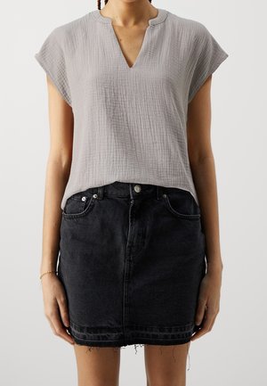 Femme portant un haut léger texturé gris clair à manches courtes avec un col en V et une mini-jupe en denim noire avec un ourlet effiloché.