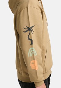 Hooded sweatshirt in tan fabric featuring black palm tree, green rainbow, and orange face graphics on the left sleeve. Casual fit with kangaroo pocket.