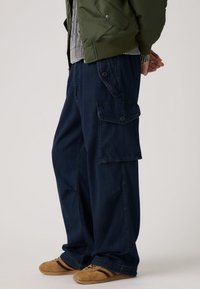 Ναυτικό μπλε cargo παντελόνια με άνετη εφαρμογή, διαθέτουν μεγάλες πλαϊνές τσέπες και διακριτικές ραφές. Συνδυάζονται με καφέ παπούτσια.