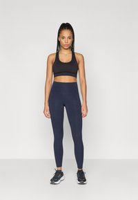 Μαύρο αθλητικό μπουστάκι και σκούρο ναυτικό κολάν από ελαστικό υλικό, με ψηλή μέση και ομαλή υφή. Μαύρα αθλητικά παπούτσια με λευκές λεπτομέρειες.