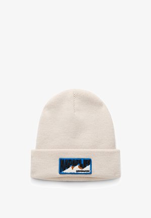 Berretto a maglia crema con risvolto e una toppa rettangolare blu con grafiche di montagne e il testo "NAPAPIJRI" in caratteri in grassetto.