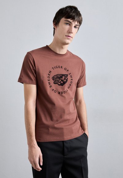 T-shirt in cotone marrone con grafica di una tigre nera e testo circolare "Tiger of Sweden". Collo a giro e maniche corte.