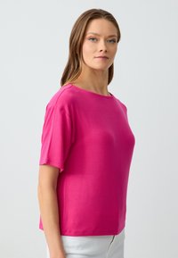 T-shirt a maniche corte, con collo rotondo, di colore rosa brillante, realizzato in tessuto morbido, caratterizzato da una vestibilità comoda e senza motivi o decorazioni visibili.
