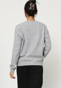 Sweater en tricot gris à manches longues, col rond et ourlet côtelé. Texture lisse avec une coupe classique, porté avec un pantalon noir.