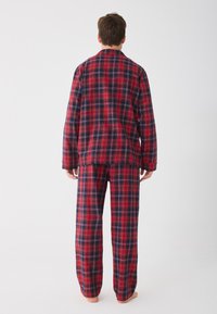 Piros és sötétkék kockás flanel pizsama szett, hosszú ujjú felsővel és laza fazonú nadrággal. Puha tapintás, klasszikus kockás minta.