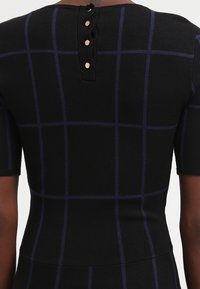 Robe en tricot noire avec motif à carreaux bleus, manches courtes et fermeture à trois boutons dorés au dos. Tissu texturé avec une silhouette ajustée.