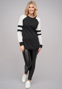 Chemise noire à manches longues avec des manches raglan grises et deux rayures noires. Associée avec des leggings en cuir noirs et des baskets blanches.