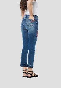 Modré riflové nohavice s kvetinovou výšivkou na boku, s úzkym strihom a ošúchaným lemom. V kombinácii s čiernymi sandálmi so remienkami.