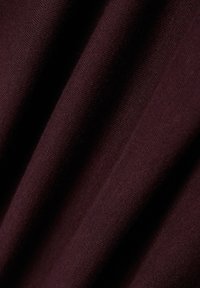 Burgunderfarbener Stoff mit weicher Textur, der ein geripptes Muster aufweist und leicht fällt. Das Material wirkt leicht und langlebig.