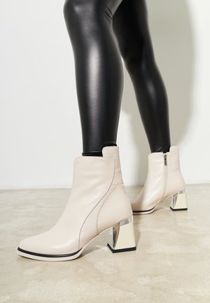 Beige ankle boots with ribbed detail on the side, square silver block heels, and a zipper closure on the back. Smooth leather texture.