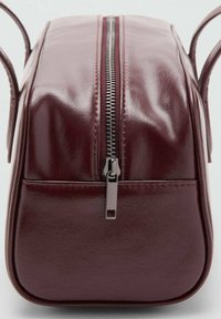 Geantă cosmetică din piele ecologică vișinie, cu formă dreptunghiulară, închidere cu fermoar și două accesorii de mânere pe fiecare parte. Textură netedă, margini cusute.