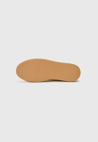 Semelle de chaussure en caoutchouc, marron clair avec des rainures horizontales pour l'adhérence, bout arrondi, texture lisse et design épuré et minimaliste.