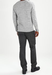 Szary sweter dzianinowy o fakturowanym wykończeniu, zestawiony z ciemnoszarymi spodniami z mieszanki wełny. Czarne buty dopełniają stylizację.