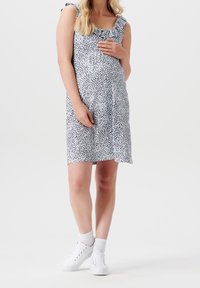 Bílé bezrukávové šaty s černým rozptýleným potiskem, řasenými ramínky a volným střihem, doplněné bílými teniskami a kotníkovými ponožkami.