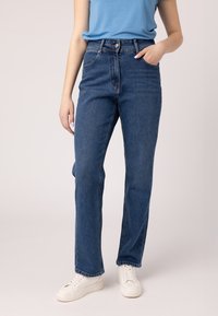 Jeans in denim blu a vita alta con taglio dritto, dotati di tasche frontali e chiusura a bottoni. Abbinati a sneaker bianche.