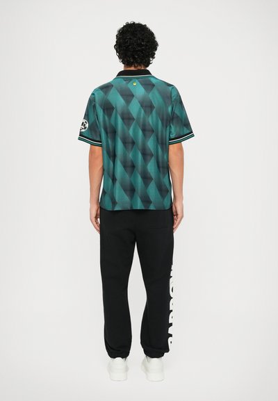 Polo à manches courtes en teal avec un motif en losanges, col noir et manches rayées. Associé à un pantalon de survêtement noir avec une marque blanche.