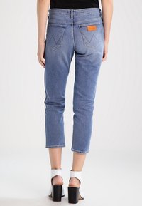 Ljusblå denimjeans med en kortad passform, med två bakfickor och en brun läderetikett. Tyget har en slät yta och en liten stretch.