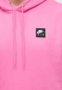 Roza kapuca iz mehkega materiala s sprednjim žepom, natančno regulirajočo kapuco in črnim kvadratnim logotipom z napisom "NIKE AIR."