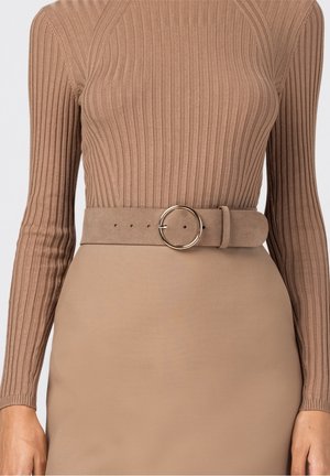 Haut beige à manches longues côtelé rentré dans une jupe assortie avec une large ceinture en daim ornée d'une boucle métallique ronde à la taille.
