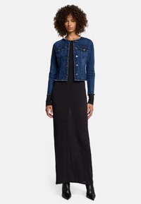 Denimjakke med en tætsiddende pasform, mørkeblå farve, forlommer og rå kant, parret med en sort maxikjole og sorte ankelstøvler.