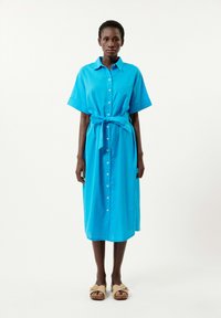 Blaues Hemdkleid mit kurzen Ärmeln, durchgängiger Knopfleiste und gebundenem Taillengürtel. Glatter Stoff mit einer einzigen Brusttasche, das bis zur Mitte der Waden reicht.