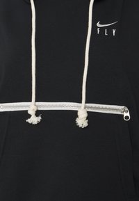 Sweat à capuche noir avec une poche zippée blanche, doté de cordons blancs avec des pompons, et un petit logo Nike blanc au-dessus de "FLY."