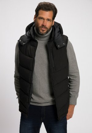 Chaleco acolchado negro con cremallera frontal y botones a presión, usado sobre un suéter de cuello alto gris claro, combinado con jeans de denim oscuro.