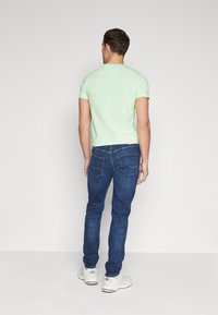 Mintgrön t-shirt med kort ärm i kombination med mörkblå jeans. T-shirten har en rund halsringning och en åtsittande design, medan jeansen har standardfickor.