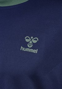Marineblauwe sportshirt met een groene kraag, voorzien van een lichtgroen logo van een bij en de tekst "hummel" aan de voorkant. Glad stofgevoel.