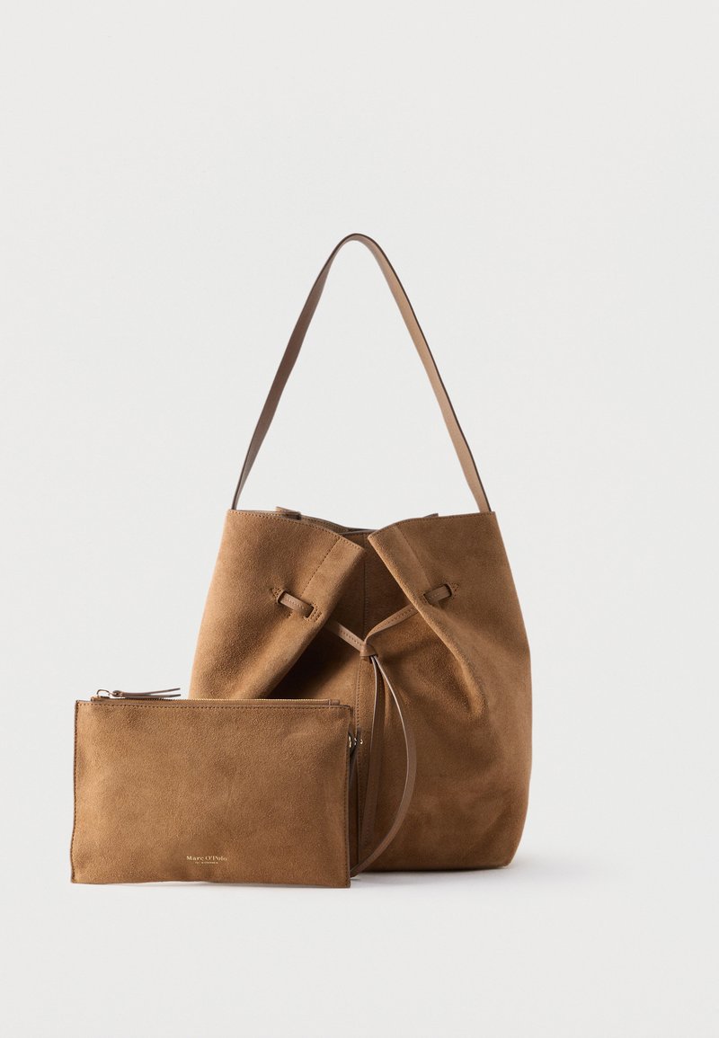 Καφέ τσάντα κουβά από σουέντ με ταιριαστό τσαντάκι με φερμουάρ, μονή λαβή ώμου και κλείσιμο με κορδόνι, σε λευκό φόντο.