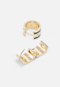 Guldtonade örhängen med en böjd design och en svart accent, slät yta och en säker låsmekanism. Ett örhänge visas öppet.