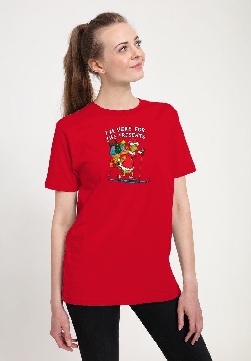 Rød bomulds T-shirt med et grafisk billede af en fantasifuld karakter, der står på ski med gaver og teksten "JEG ER HER FOR GAVERNE" ovenfor.