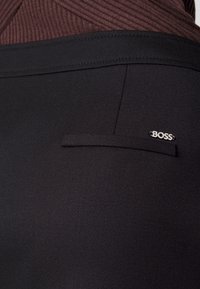 Svarta skräddarsydda byxor har en slät textur, en liten sidoficka med en horisontell flik och en silverfärgad 'BOSS'-logotyp som accent.