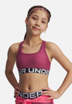 Prepuber meisje met gevlochten haar en een roze haarband, draagt een roze sport-bh en bijpassende legging, handen in de heupen, kijkt naar de camera.