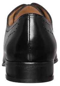 Chaussure habillée en cuir noir avec un bout arrondi, une finition lisse, des perforations décoratives et un talon empilé. Couture visible le long des bords.