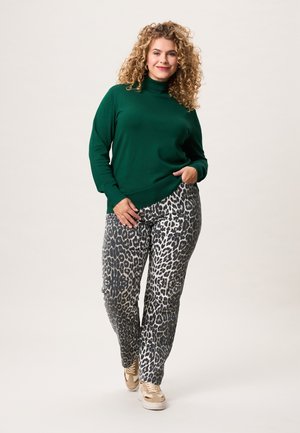 Groene coltrui gecombineerd met zwart en grijs luipaardprintbroek. De outfit wordt compleet gemaakt met beige sneakers.
