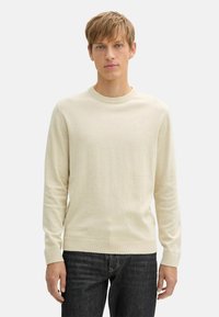 Maglione a maglia beige con collo rotondo e maniche lunghe, con polsini e orlo a coste, abbinato a jeans in denim scuro. Tessuto morbido.