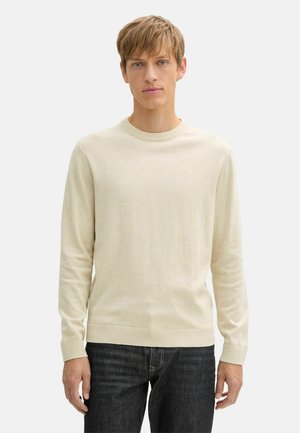 Jersey de punto beige con cuello redondo y mangas largas, con puños y dobladillo acanalados, combinado con jeans de mezclilla oscura. Textura suave.