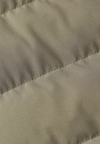 Tessuto verde oliva testurizzato con una finitura liscia, caratterizzato da linee di cucitura diagonali e leggere ondulazioni, che indicano un design imbottito.