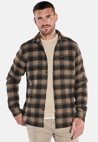 Brown and black plaid shirt in a soft texture, with a button-up design and collar, layered over a light ribbed sweater.