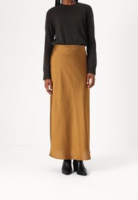 Lange, mosterdgele rok gemaakt van gladde stof, gecombineerd met een donker gebreid truitje en zwarte hoge laarzen.