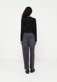 Camisa negra de manga larga combinada con jeans grises de pierna ancha. Los jeans tienen dos bolsillos traseros y una etiqueta en la cintura. Botas negras de plataforma visibles.