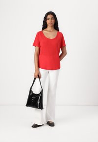 Top rosso a maniche corte con scollatura a barca, abbinato a pantaloni bianchi a palazzo. Borsa in pelle nera con dettaglio a fibbia e scarpe nere basse.