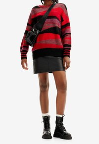 Pull rayé multicolore en rouge, noir et gris ; poignets et ourlet côtelés. Mini-jupe noire en cuir avec plis. Bottes noires lacées.