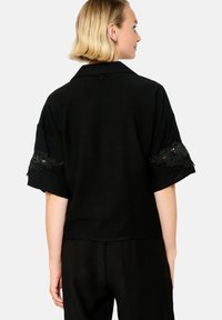 Blusa nera a maniche corte con dettagli ricamati sulle maniche, texture liscia e colletto. Design semplice e dal fit rilassato.