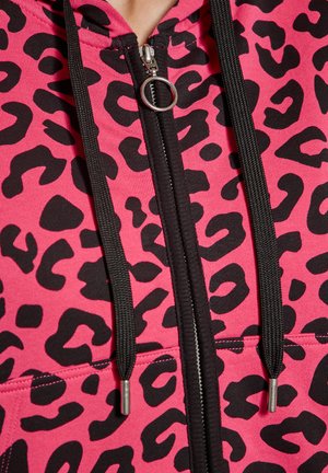 Lyserød lynlås hoodie med et sort leopardmønster, sorte snore med sølvspidser og en centralt lynlåsdetalje.