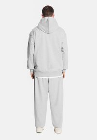 Szara bluza z kapturem o wysokim dekolcie i luźnym kroju, w zestawie z luźnymi szarymi spodniami dresowymi. Materiał wydaje się miękki i strukturalny.
