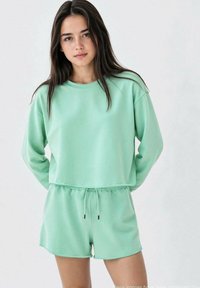 Completo loungewear verde menta realizzato in tessuto morbido, composto da una maglietta a maniche lunghe dal taglio rilassato e pantaloni corti con vita elastica e dettagli con coulisse.